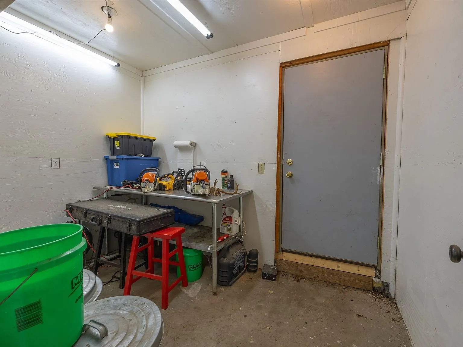 A utility storage room with chainsaws and gear near a side door