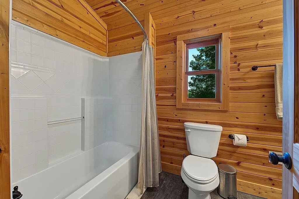 A bathroom with a tub-shower combination and wood paneling