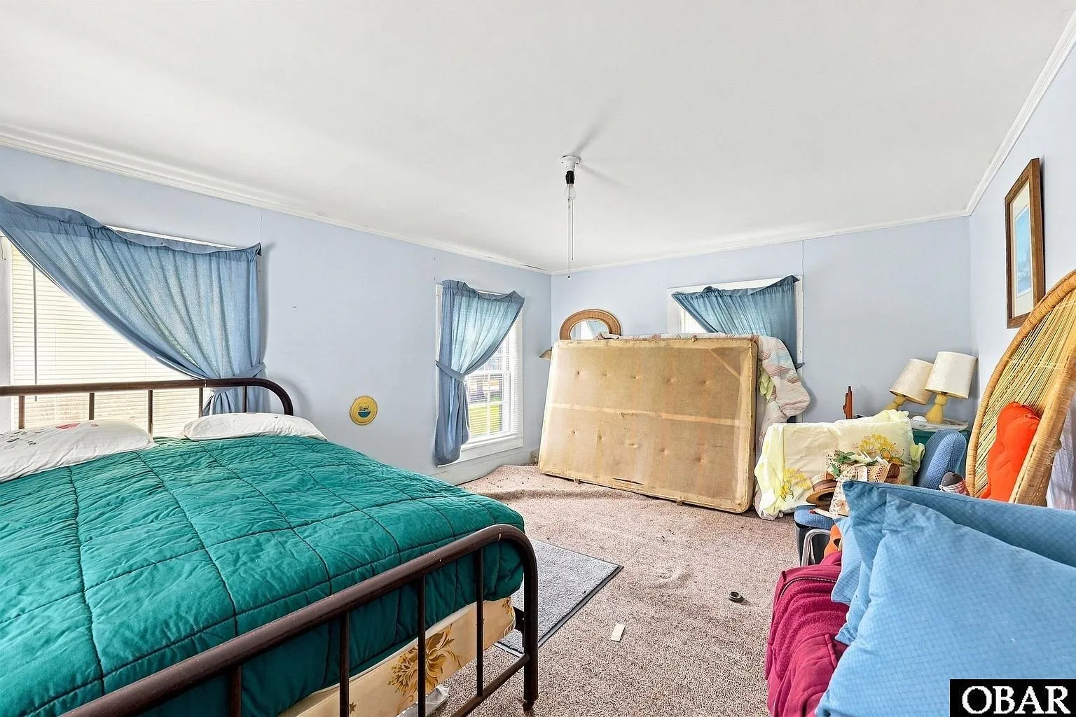 An upstairs bedroom with an iron bed and blue curtains