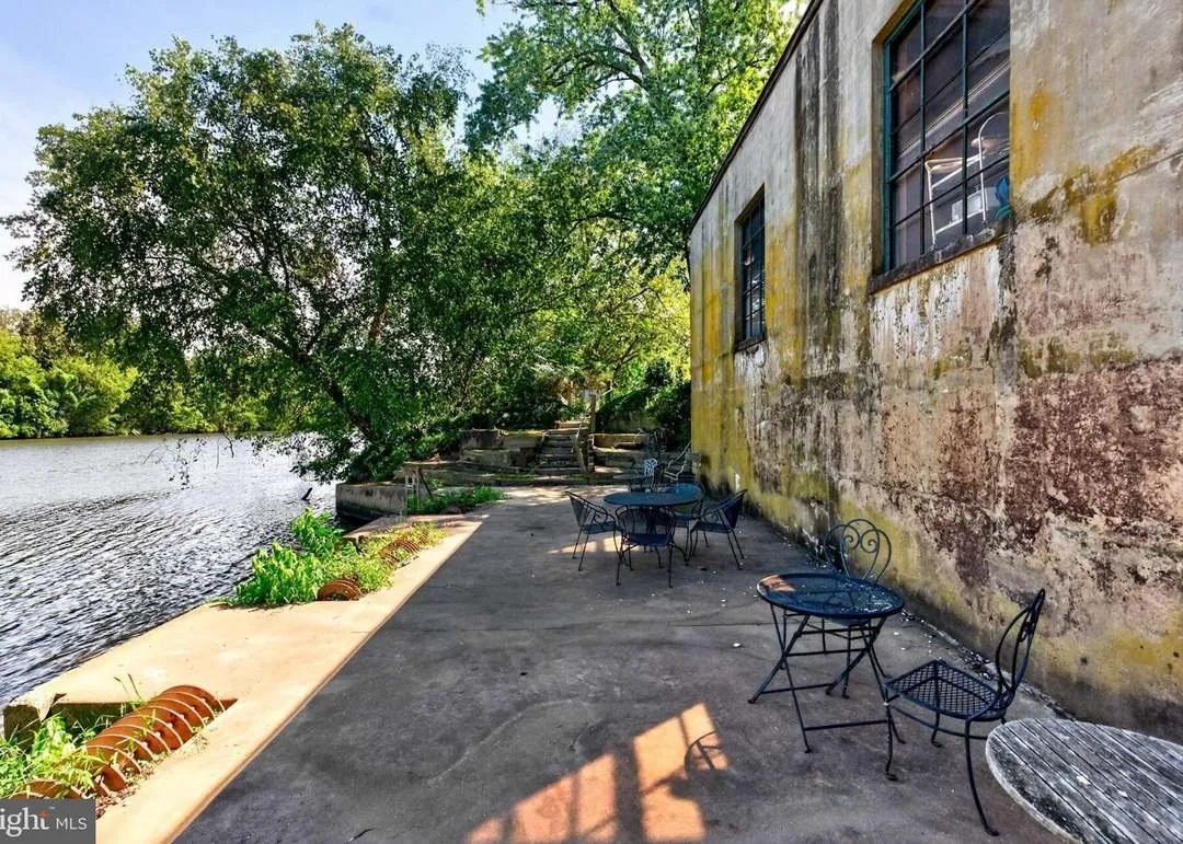 A stone patio with outdoor seating along the building's river-facing wall