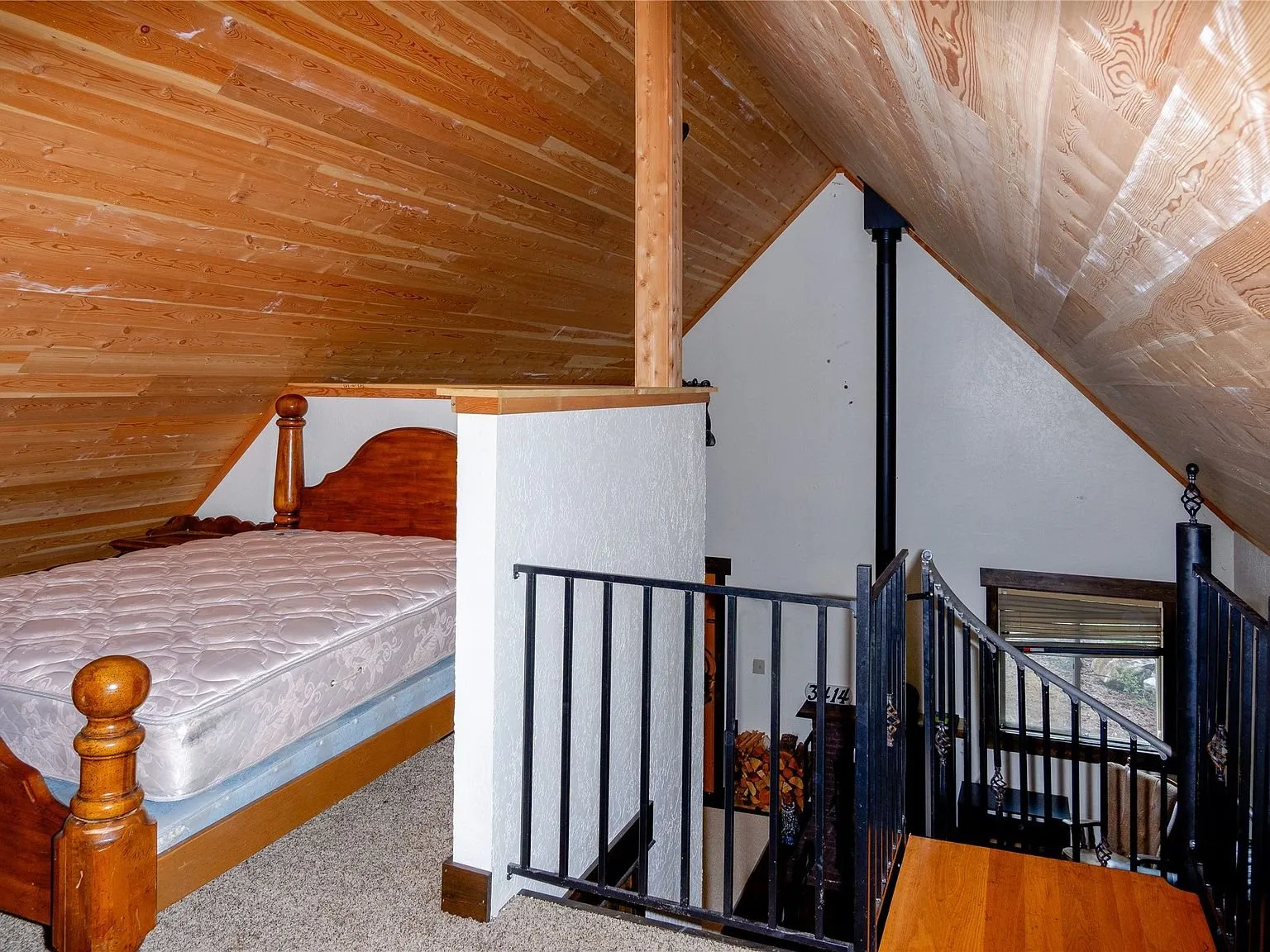 A bed tucked into the loft beside the open stair rail
