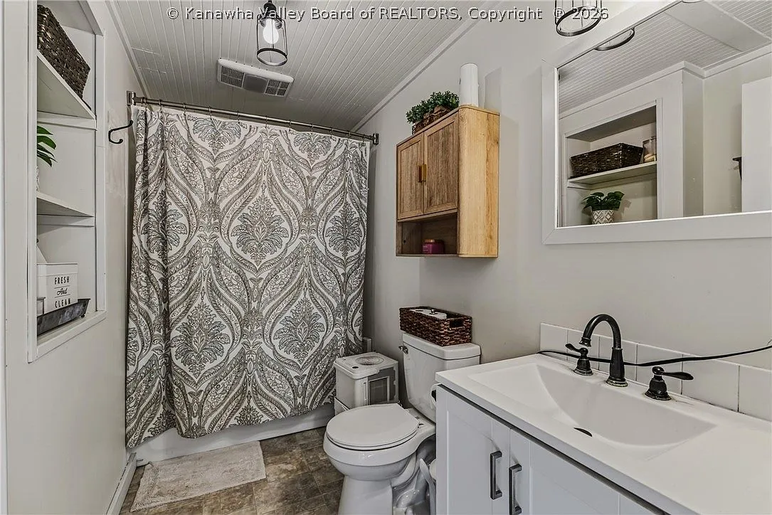 A full bathroom with a patterned shower curtain and wood storage cabinet