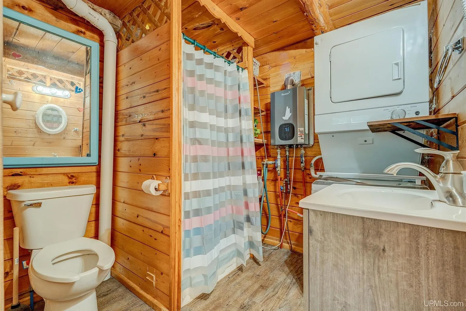 The bathroom with toilet, shower curtain and stacked washer and dryer