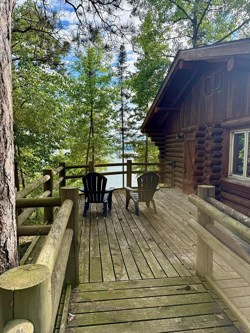 The deck along the cabin with the chairs and the lake beyond