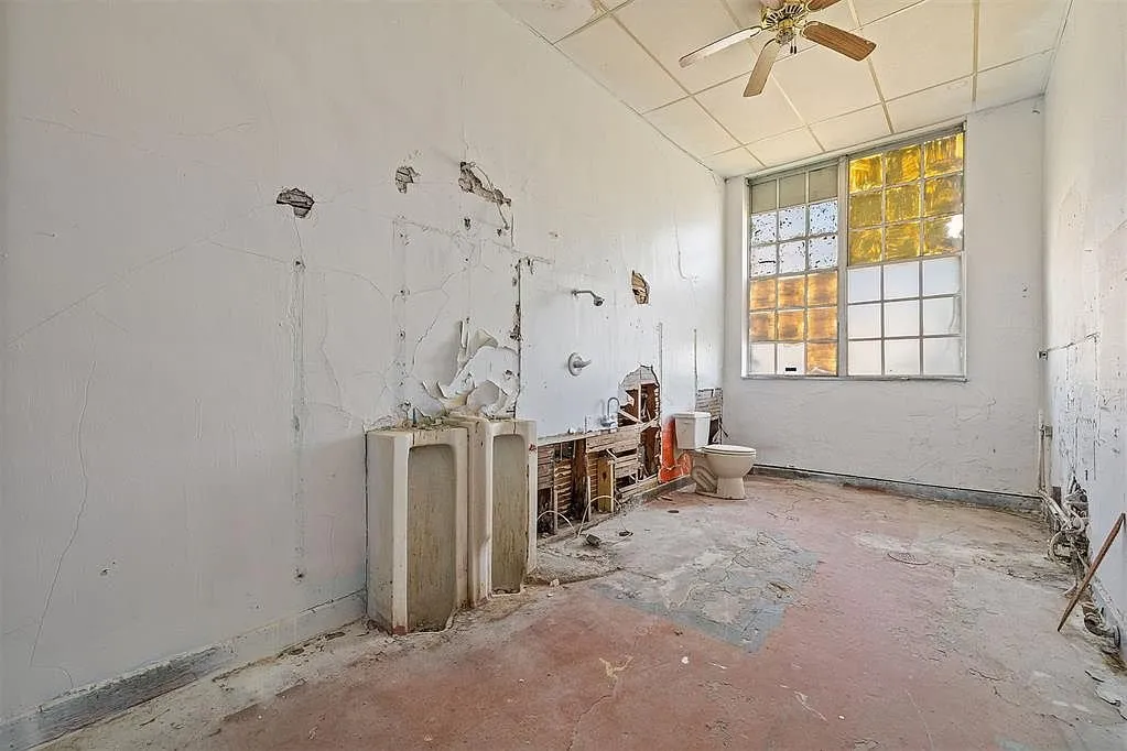The stripped restroom with the sinks and the toilet under the window