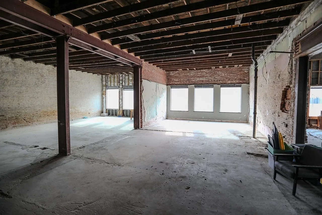 A stripped room with windows at the far end and bare concrete floor