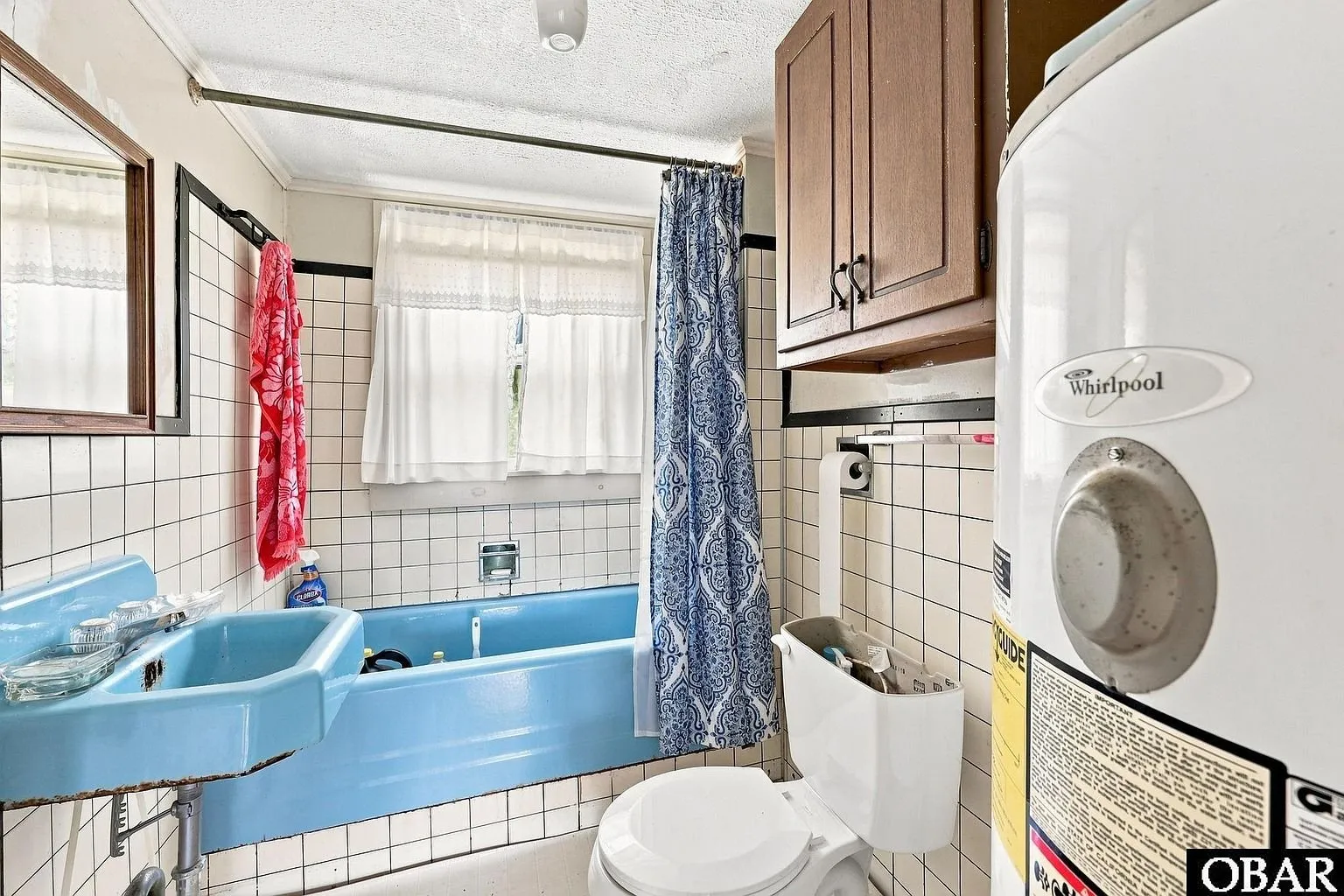 The bathroom with blue fixtures, a tub and the water heater in the corner