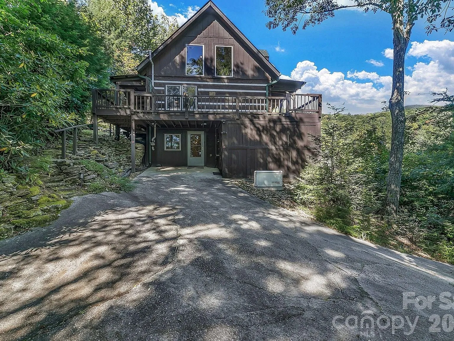 The cabin seen from the gravel driveway, decks stacked above the carport level