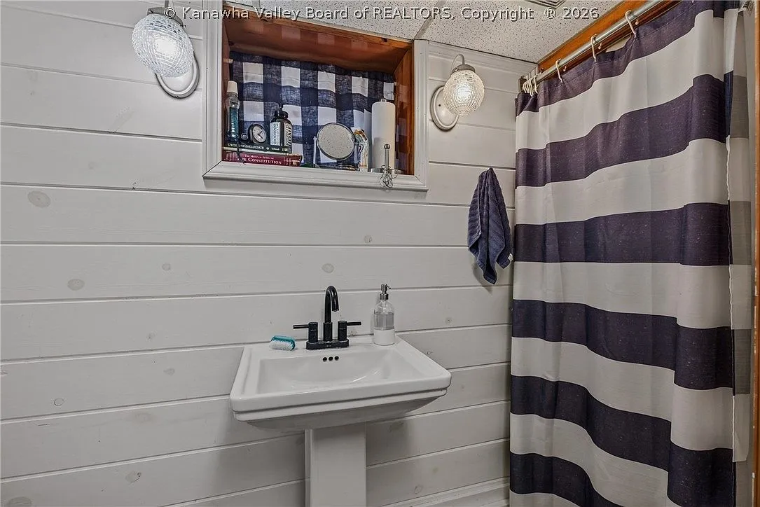A basement half bathroom with a pedestal sink and striped shower curtain
