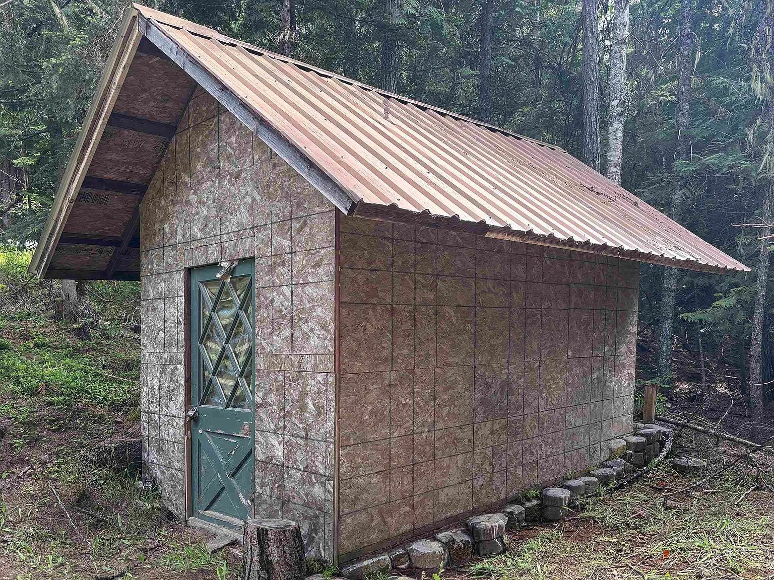 The outhouse structure, built of weathered wood, tucked among the trees