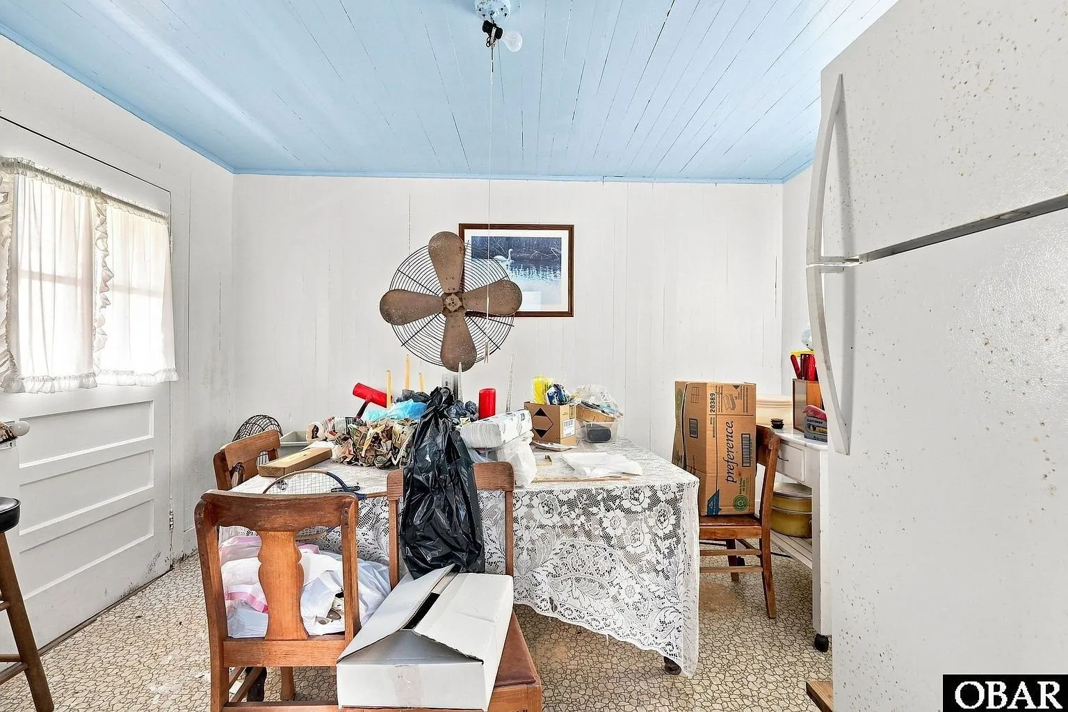 The kitchen with a fan, refrigerator and cluttered table