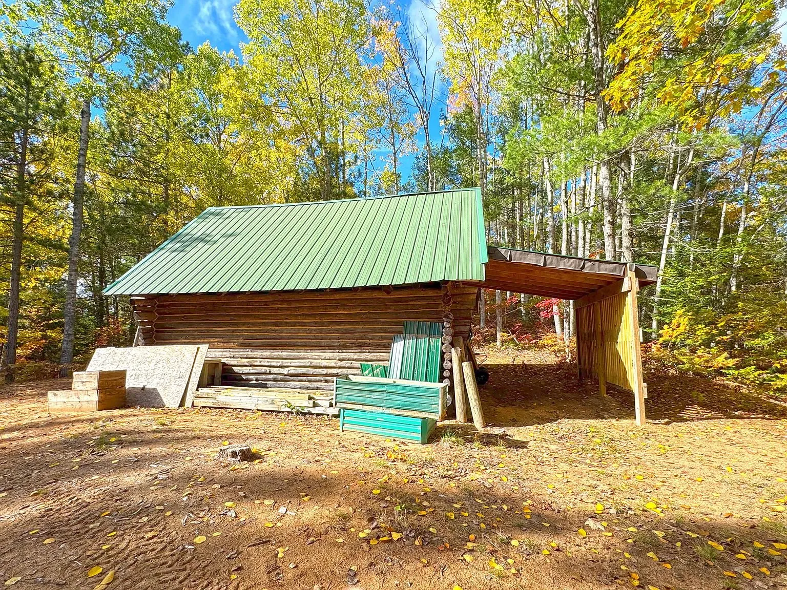The log garage from the side, green metal roof and stacked timber