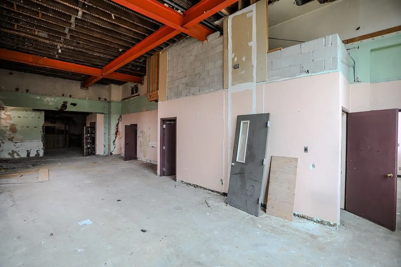 An upper floor room with steel beams overhead and partitions stripped to the studs