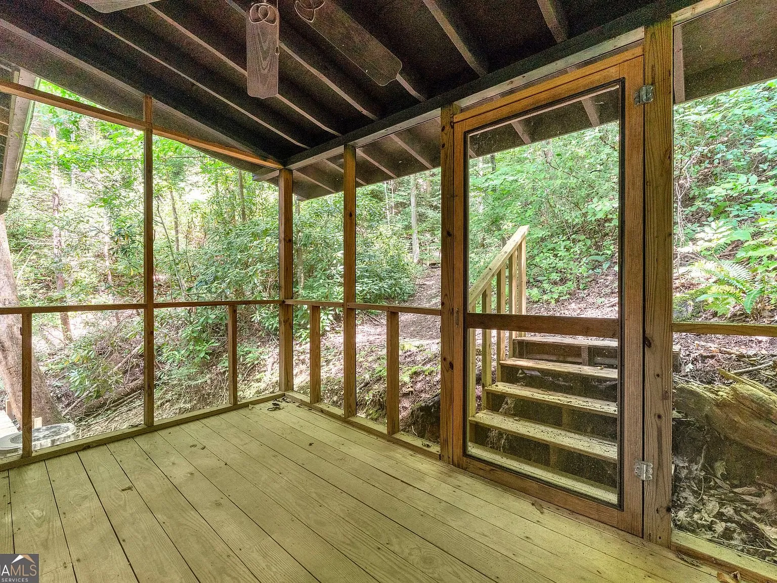 The screened porch with wood decking and stairs leading down toward the creek
