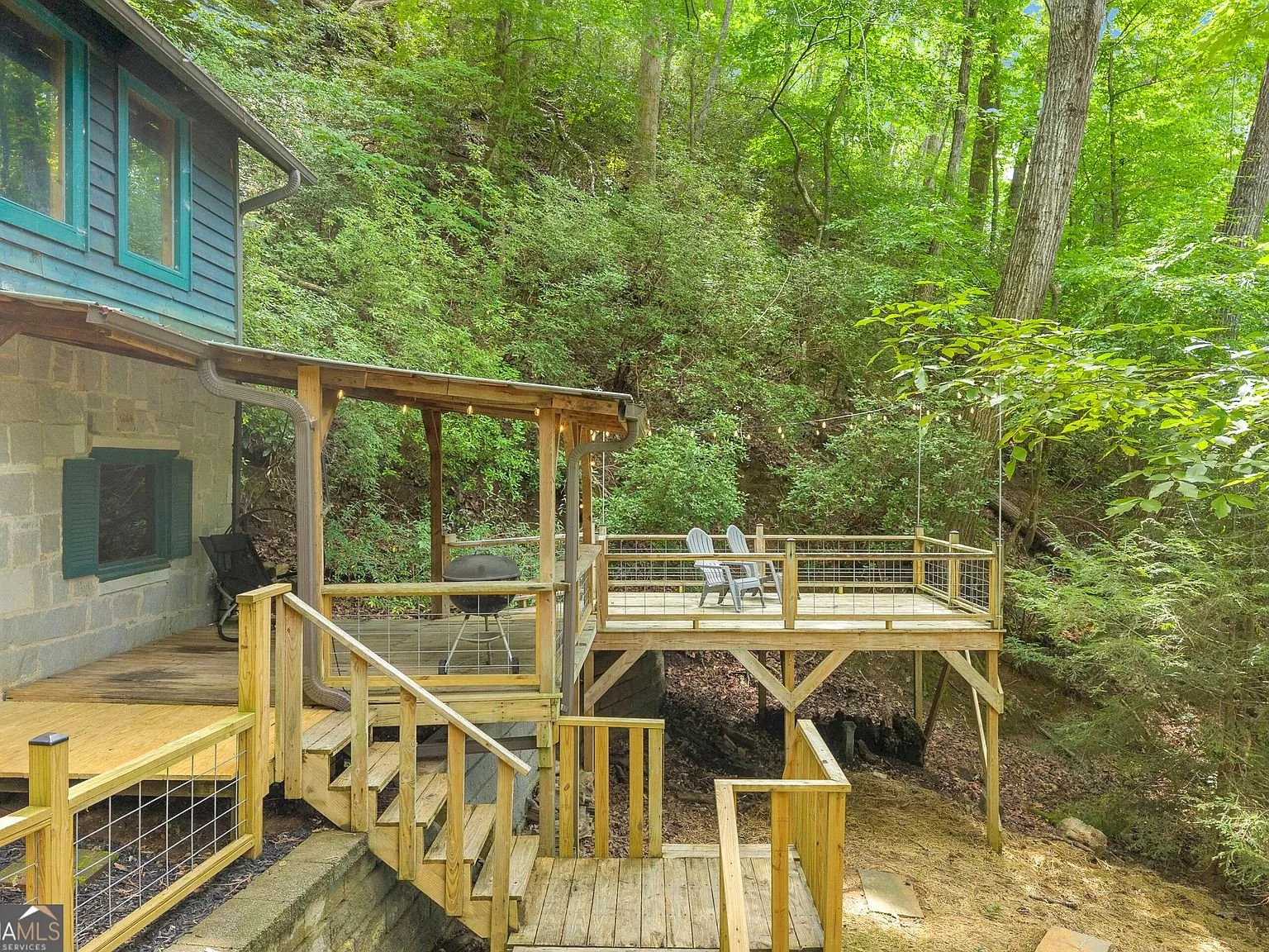 A wood deck with stairs descending toward the wooded creek bank