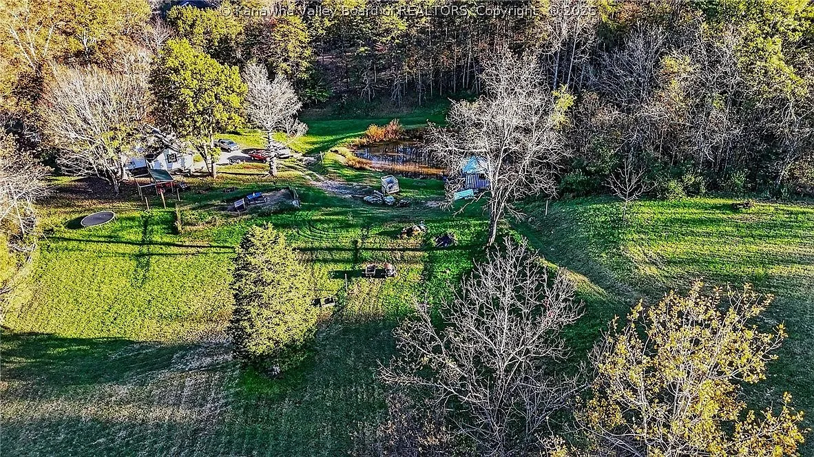 An aerial view of the pond and house framed by the tree-lined hillside