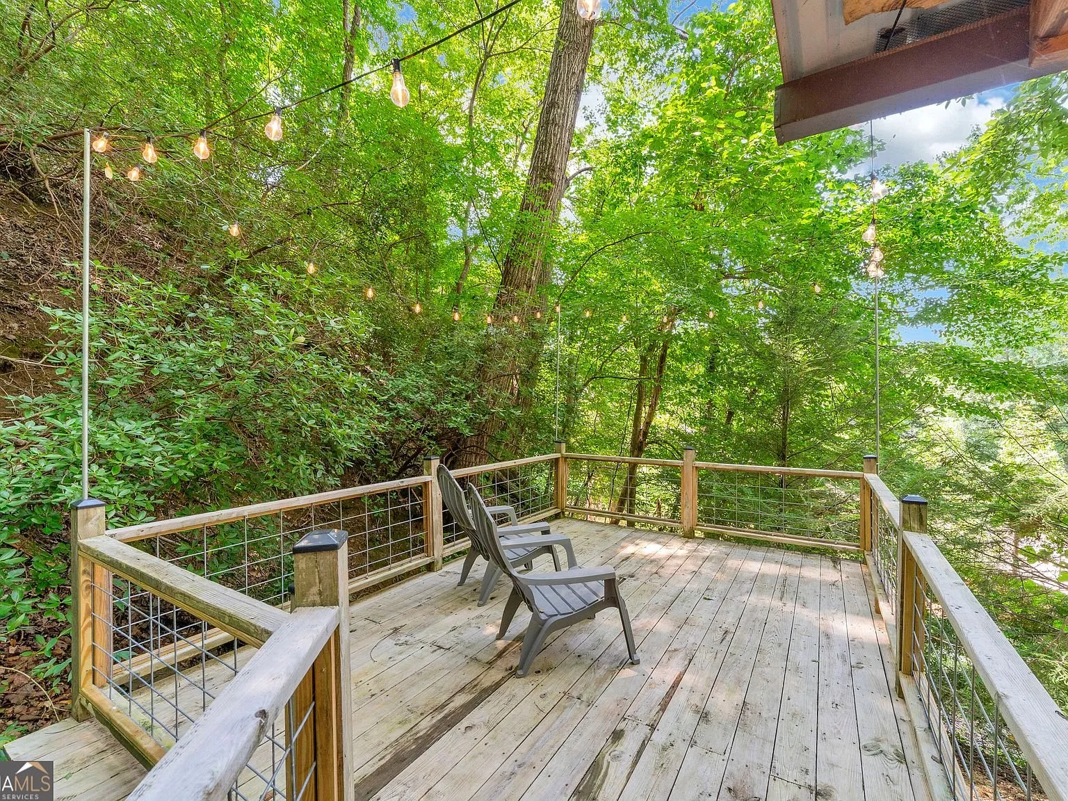 A deck with string lights and a bench seat among the trees