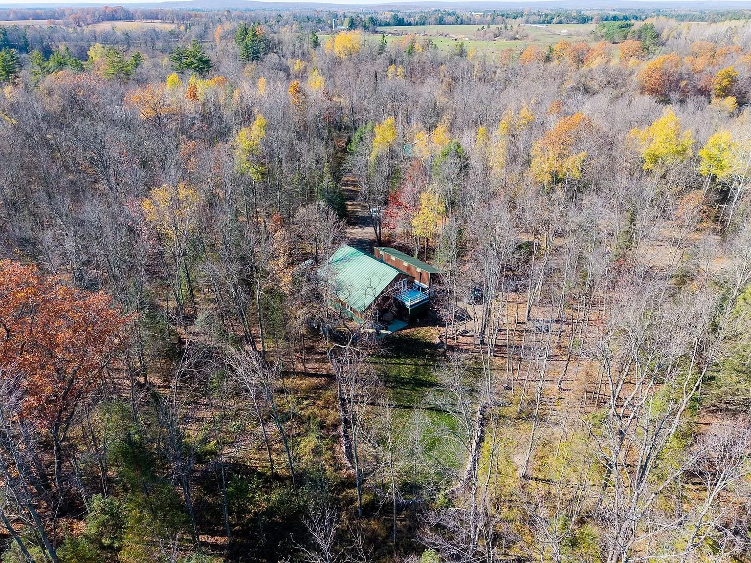 Aerial view of the home and driveway surrounded by fall-colored woods