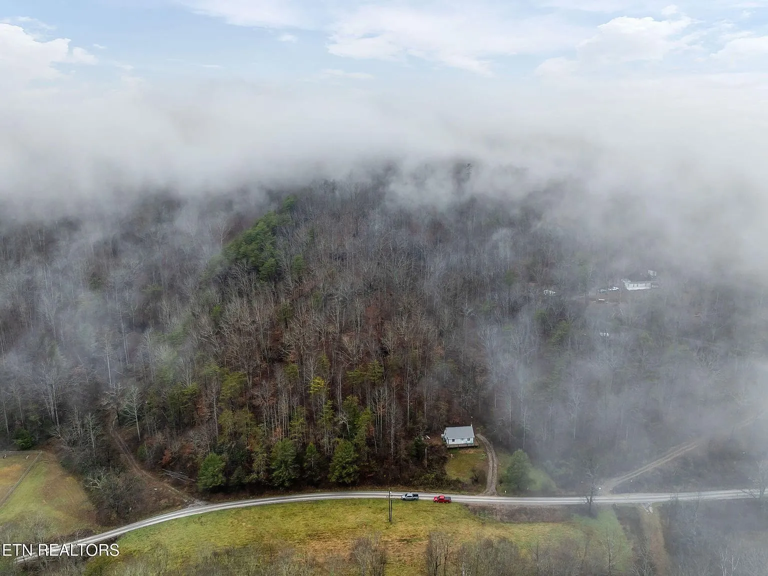 Aerial view of the wooded valley and driveway winding below the fog line