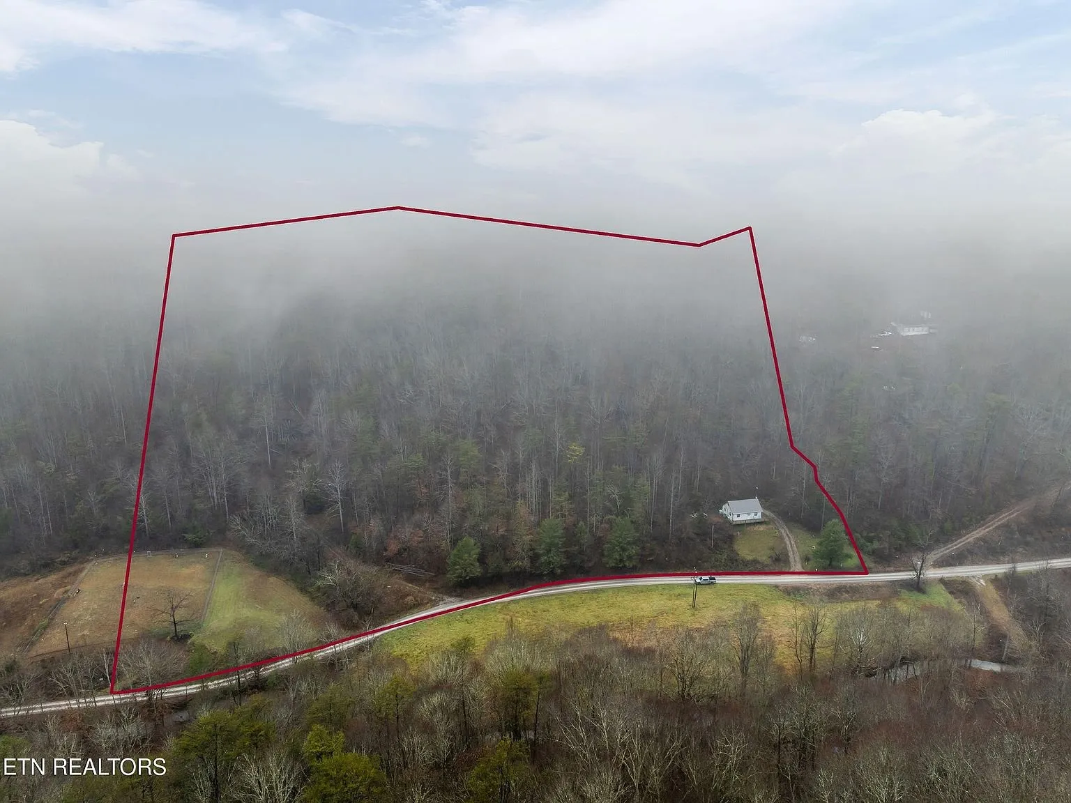 Aerial view of the driveway and clearing below the fog-covered ridge