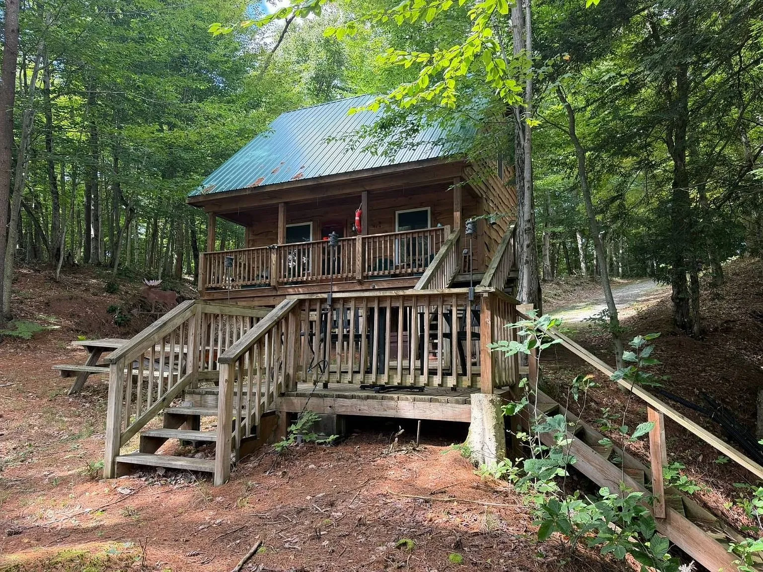 The log-sided chalet on posts with its front deck and the steps down to the drive