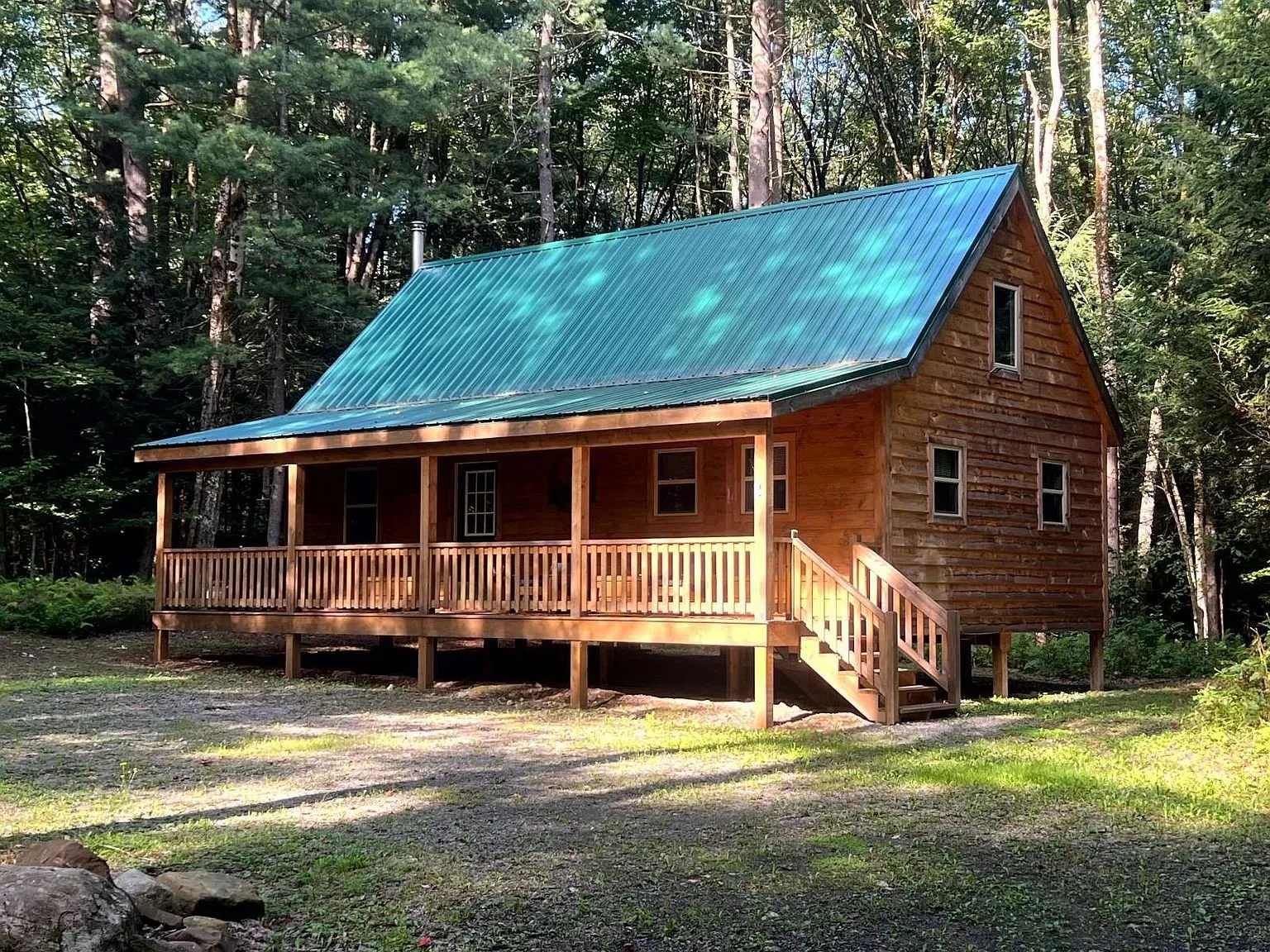 The wood-sided cabin with its green metal roof and full front porch in the trees