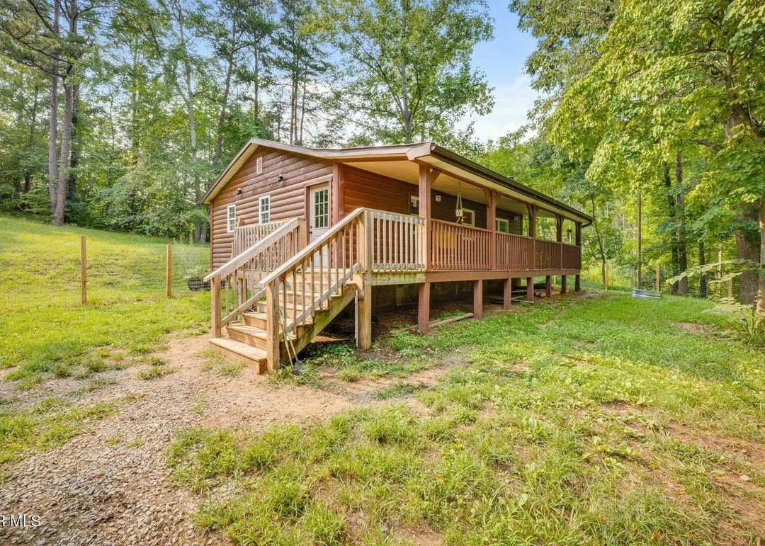 The log-sided home with a full-length covered porch, seen from the cleared yard