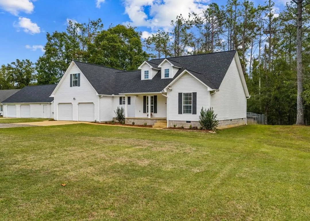 The white two-story home seen from the driveway, framed by tall pines