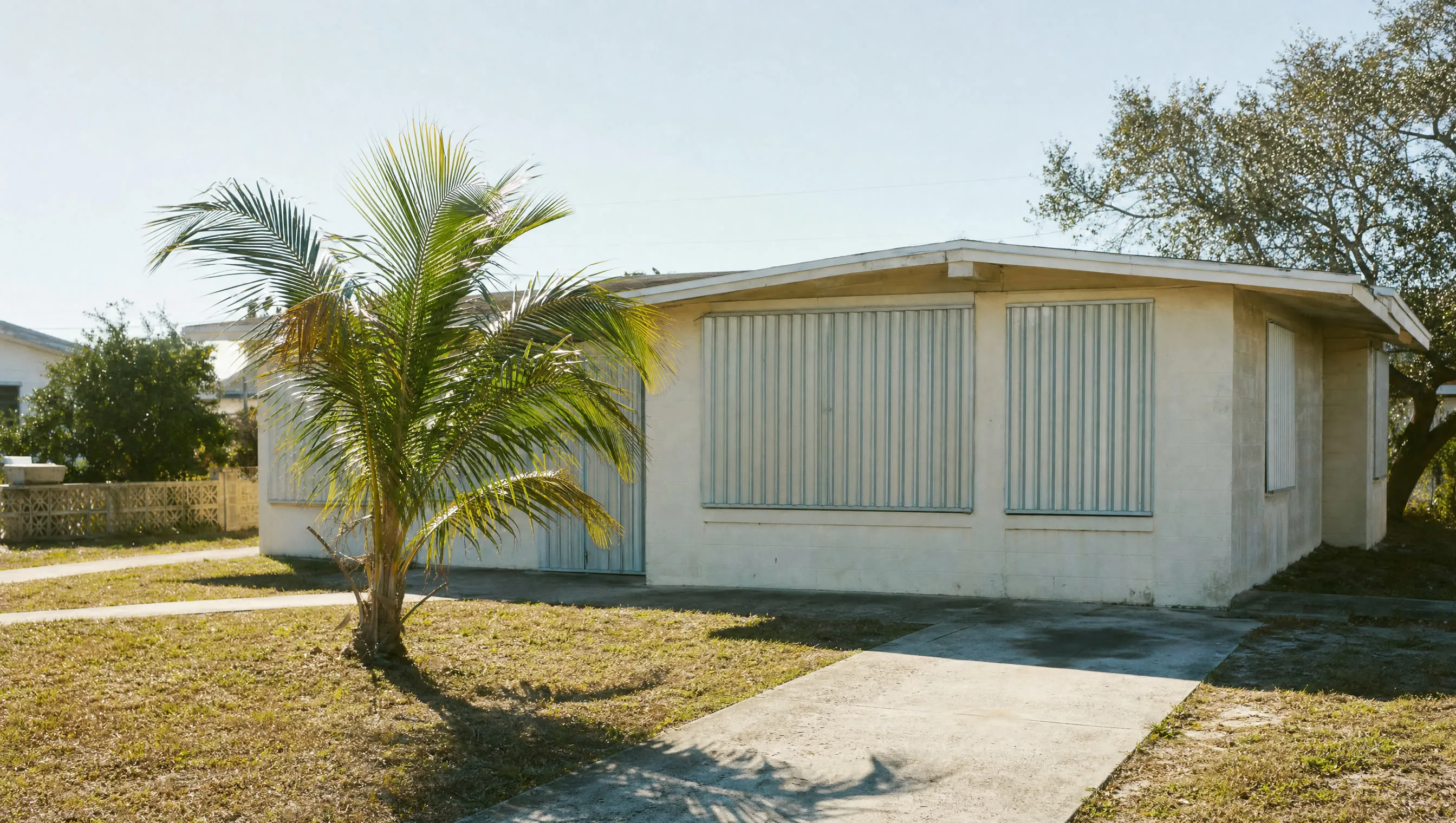 A mid-century Florida house with shutters closed in hard light