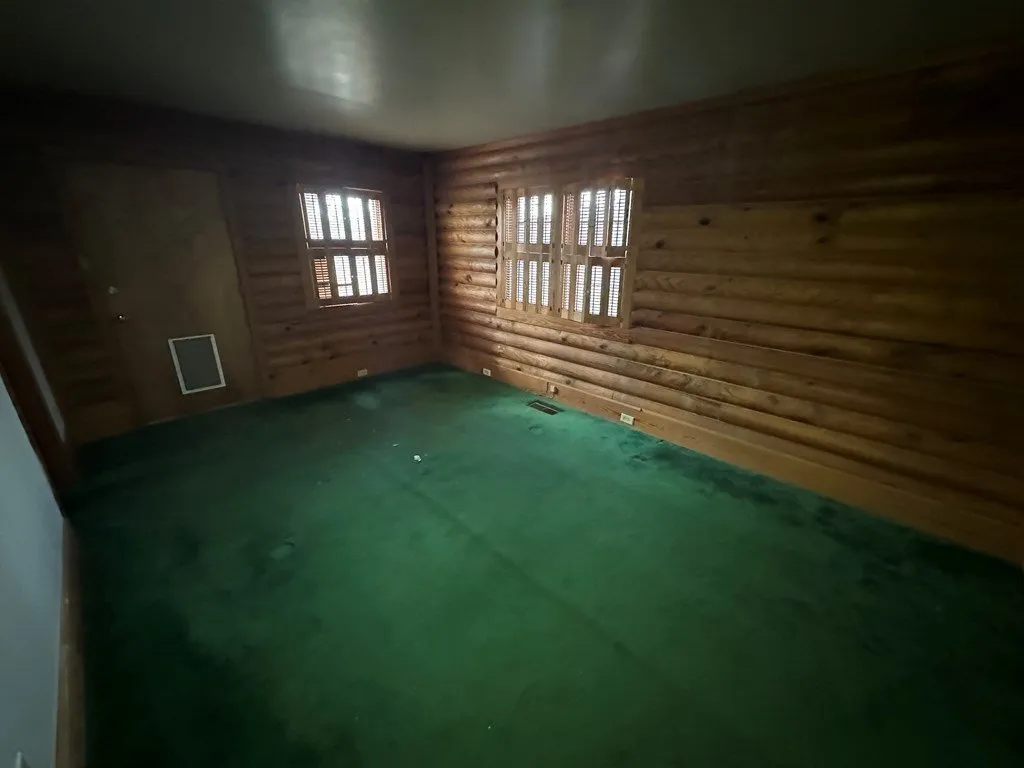 A bedroom with green carpet and log walls