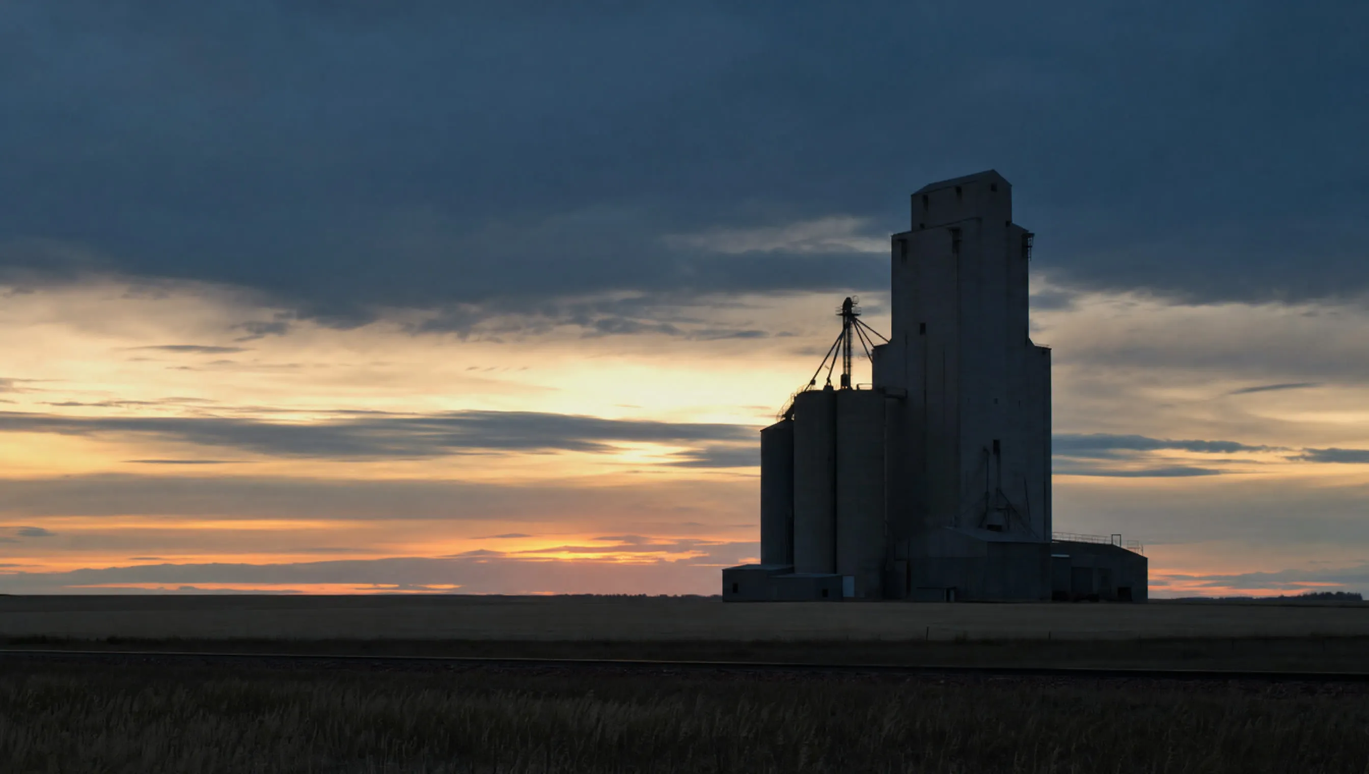 A grain elevator on a flat prairie horizon at dusk