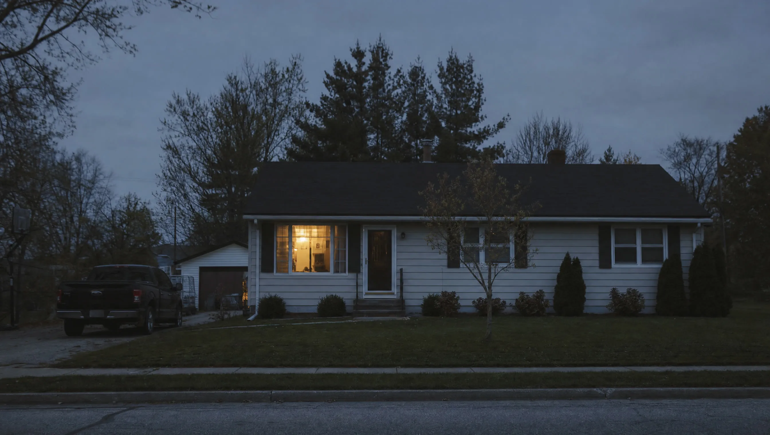 A small house at dusk with one window lit