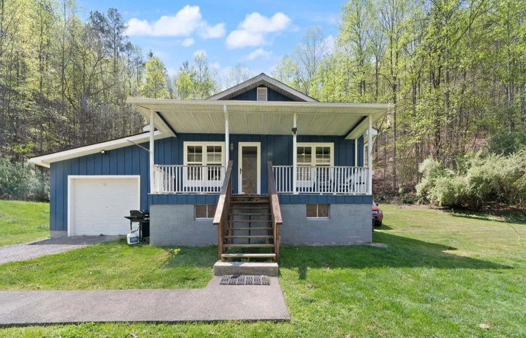 The blue house with its white garage door and front steps, ridges behind