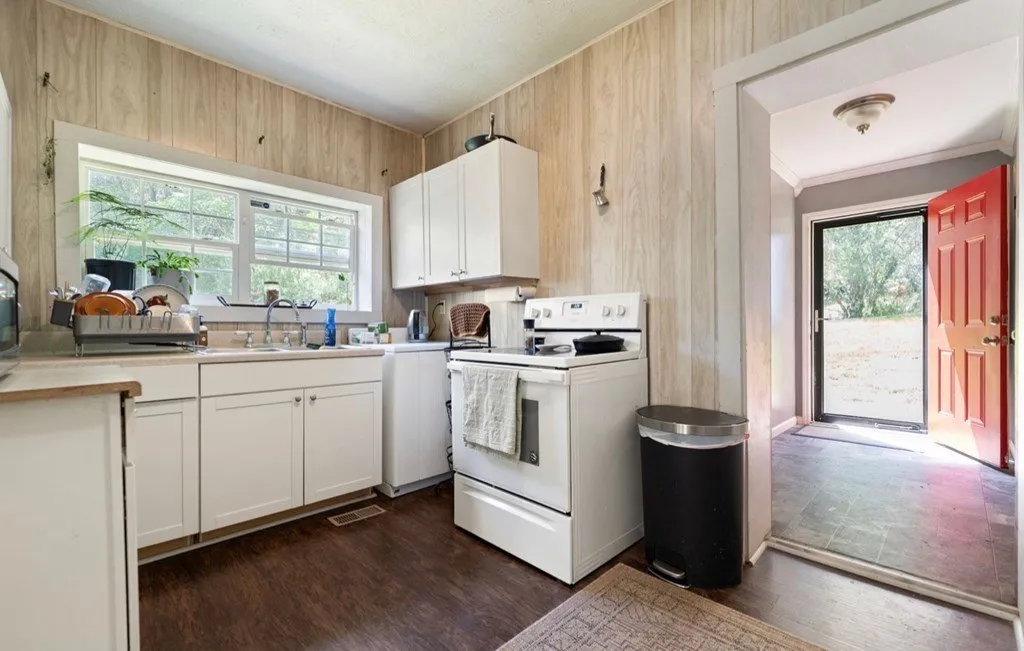 The kitchen with white cabinets, a window over the sink and the red front door beyond