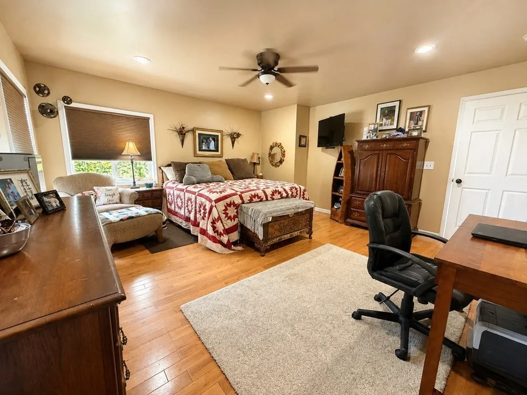 A bedroom with a quilted bed, wood floors and a desk under the window