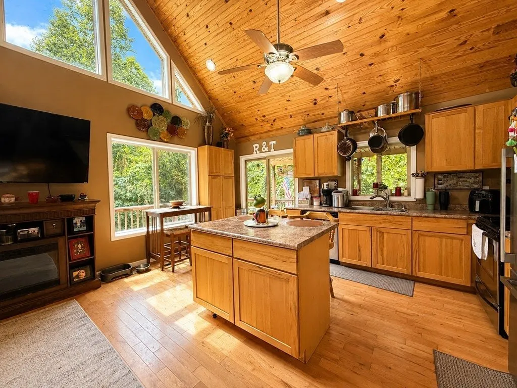 The kitchen with an island, wood cabinets and stainless appliances under the vaulted ceiling