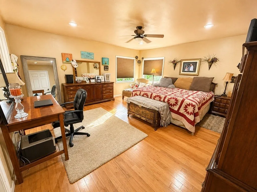 A bedroom with a quilt, a desk and wood floors