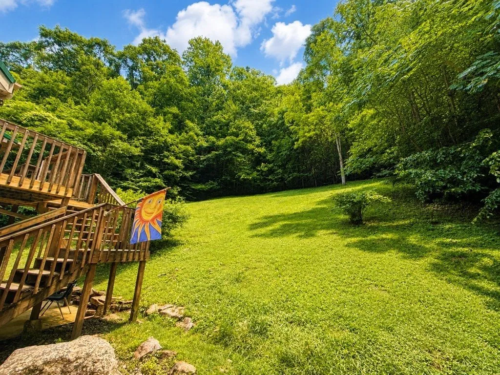 The lawn beside the house, deck stairs on the left and woods all around
