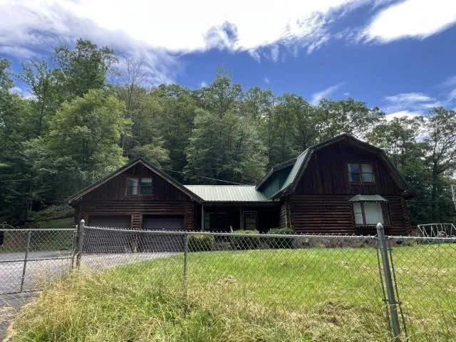 The log house behind a chain-link fence, gambrel roof and green metal roofing