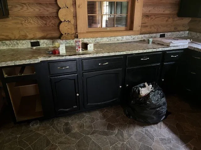 The kitchen with dark cabinets and granite counters, a trash bag on the floor