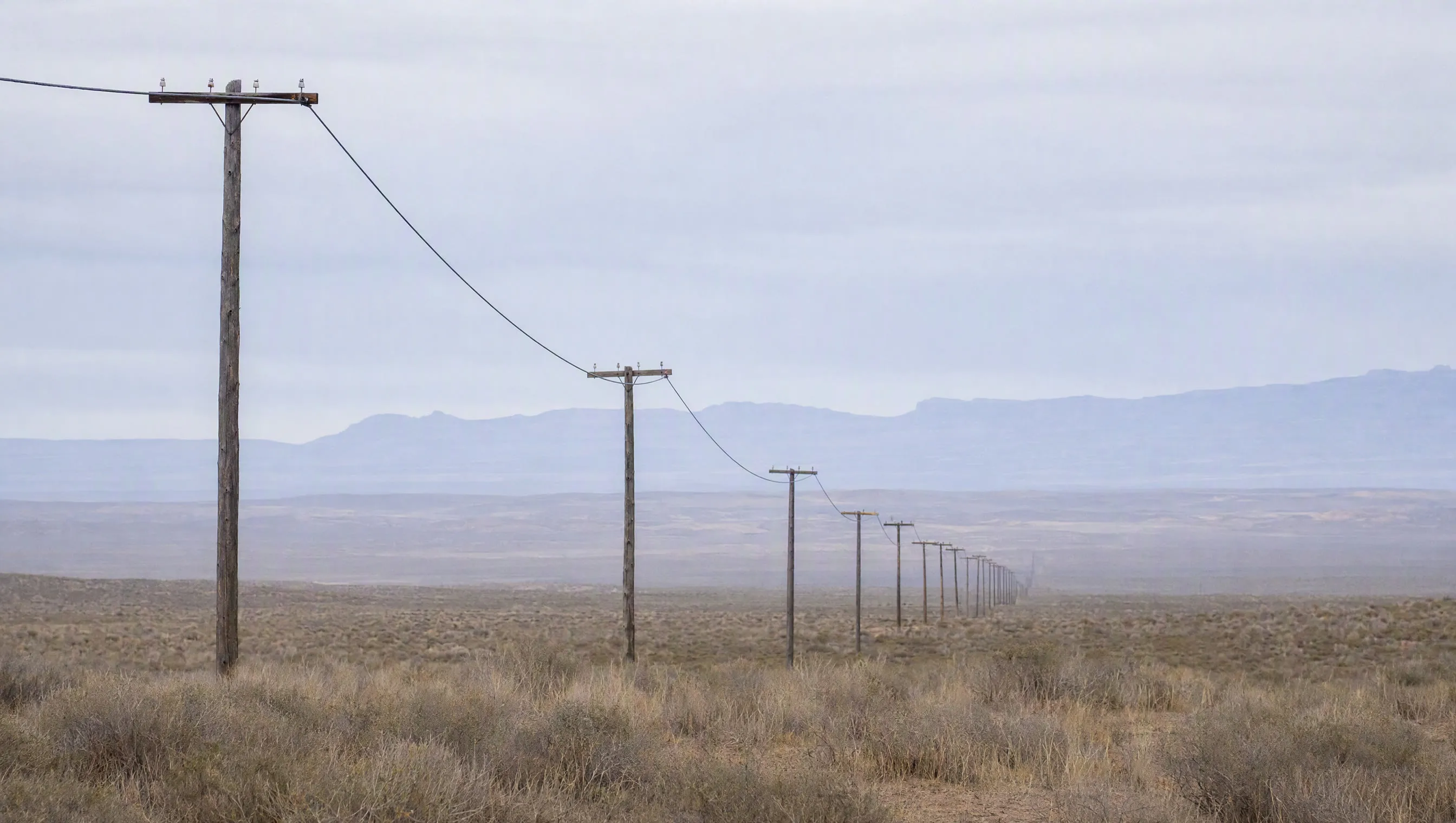 A power line crossing empty land toward the horizon