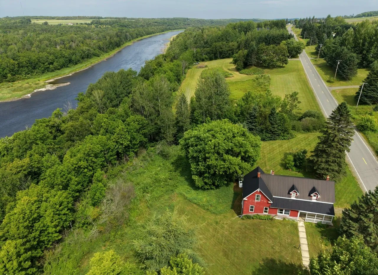 Aerial of the red farmhouse in its clearing, the road running past toward the river