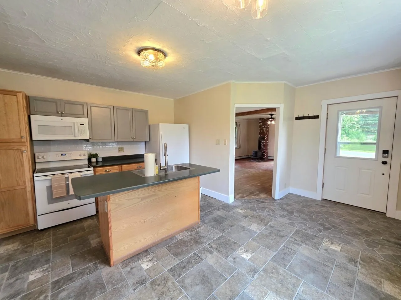 The kitchen with grey cabinets, a wood-fronted island and a doorway through to the den