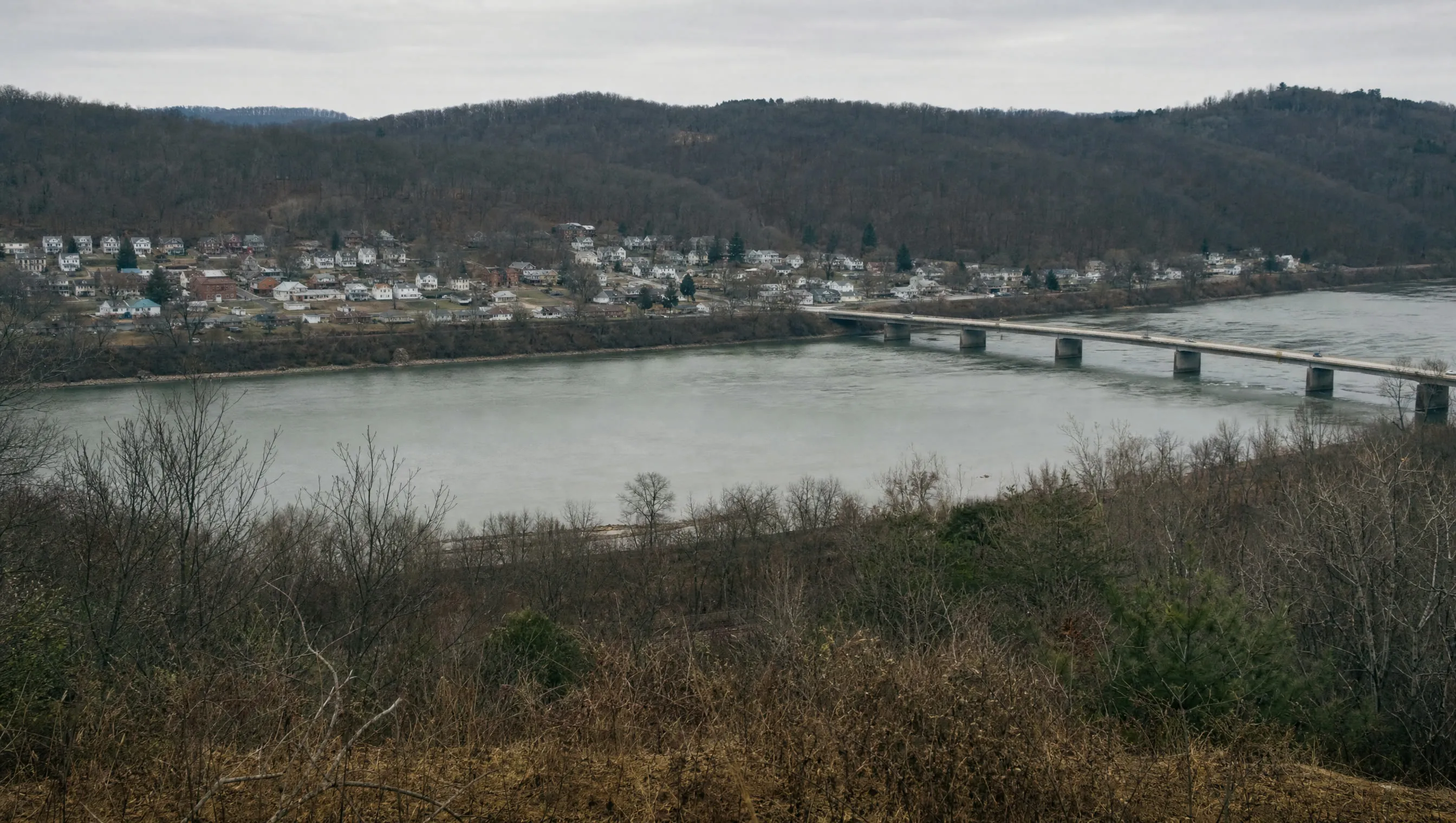 A river town of modest houses and a road bridge seen from the hillside above