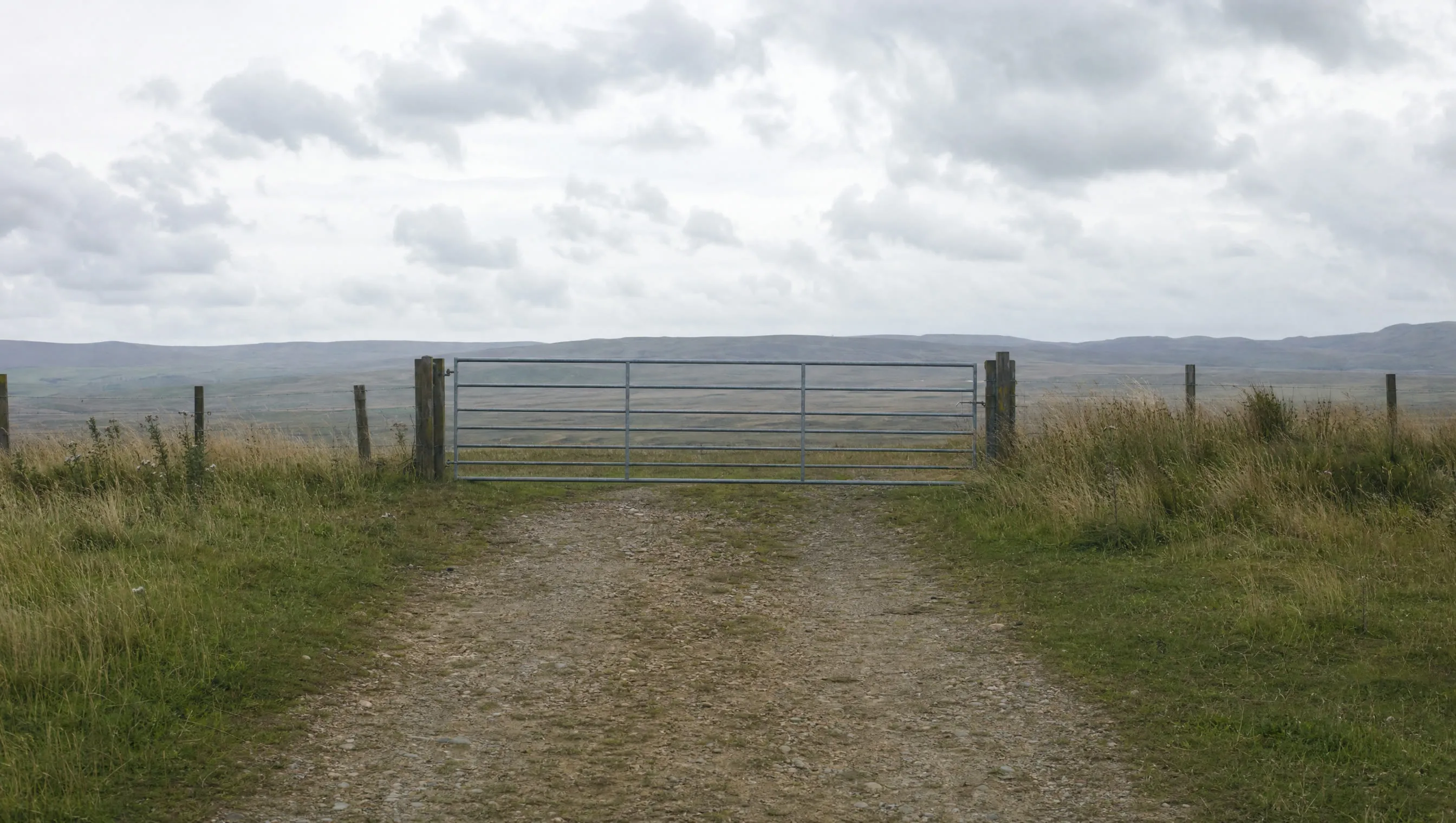 A dirt track ending at a gate in open country